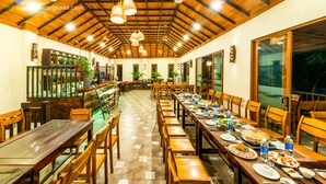 A spacious dining area with wooden tables and chairs, a long counter with a display of bottles, and a high ceiling with exposed beams. - Puluong Casa Resort (Pu Luong)