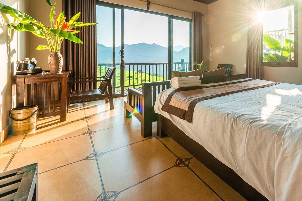 A bedroom with a large bed, a view of mountains, and a balcony with a table and chairs.