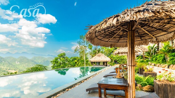A infinity pool with a view of mountains, wooden lounge chairs, and thatched umbrellas. - Puluong Casa Resort (Pu Luong)