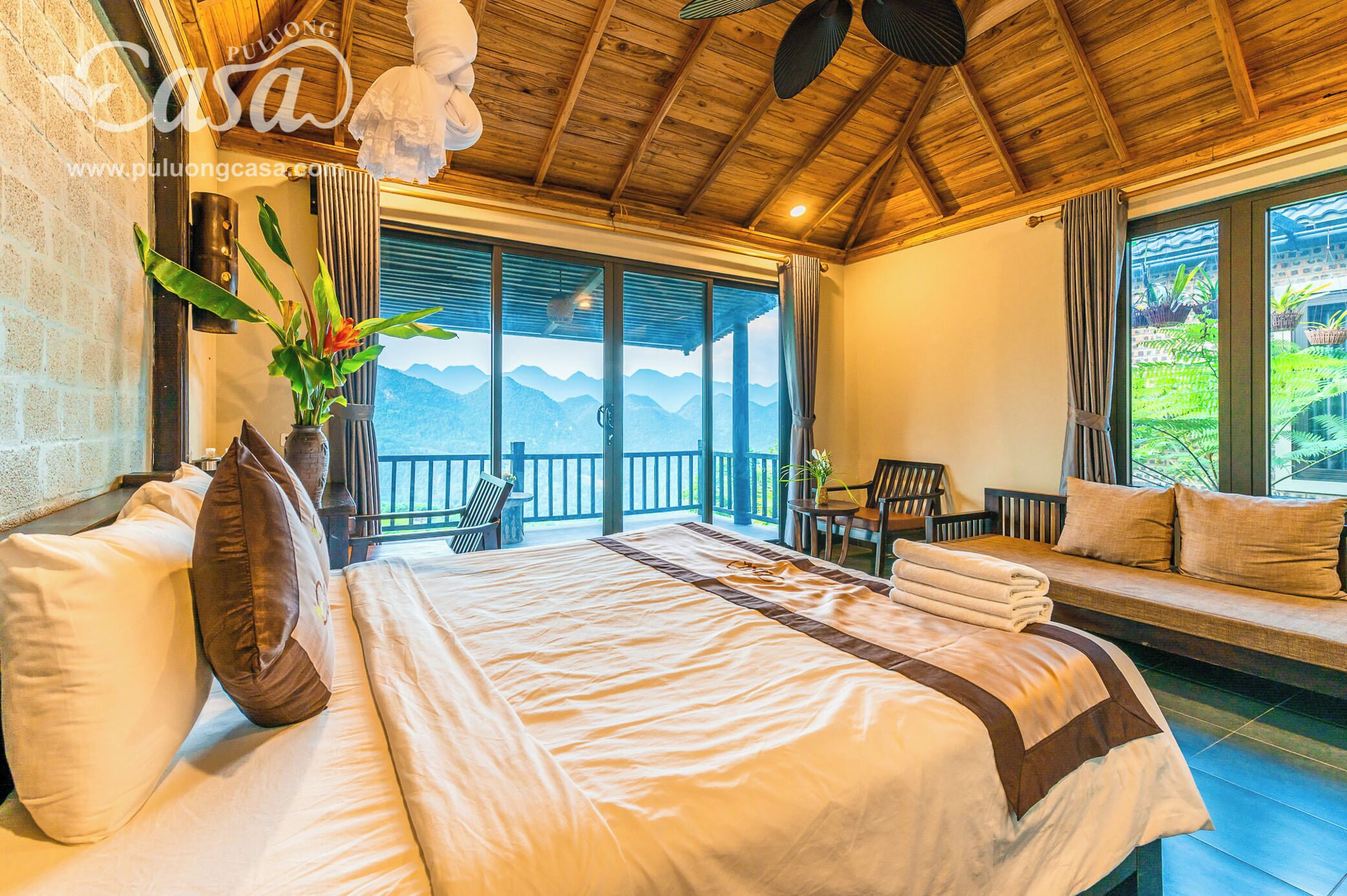 A bedroom with a large bed, a seating area with a view, and a balcony.