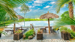 A terrace with outdoor seating, a view of a mountain range, and a thatched roof structure. - Puluong Casa Resort (Pu Luong)