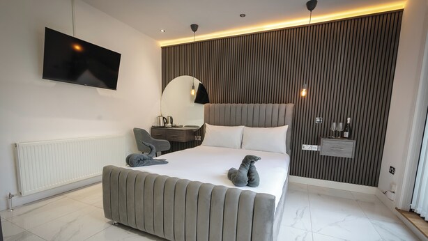 A modern bedroom with a large bed, a flat-screen TV, a bedside table with a lamp, and a wall-mounted mirror. - OYO Bellevue Apartments Middlesborough (Middlesbrough)