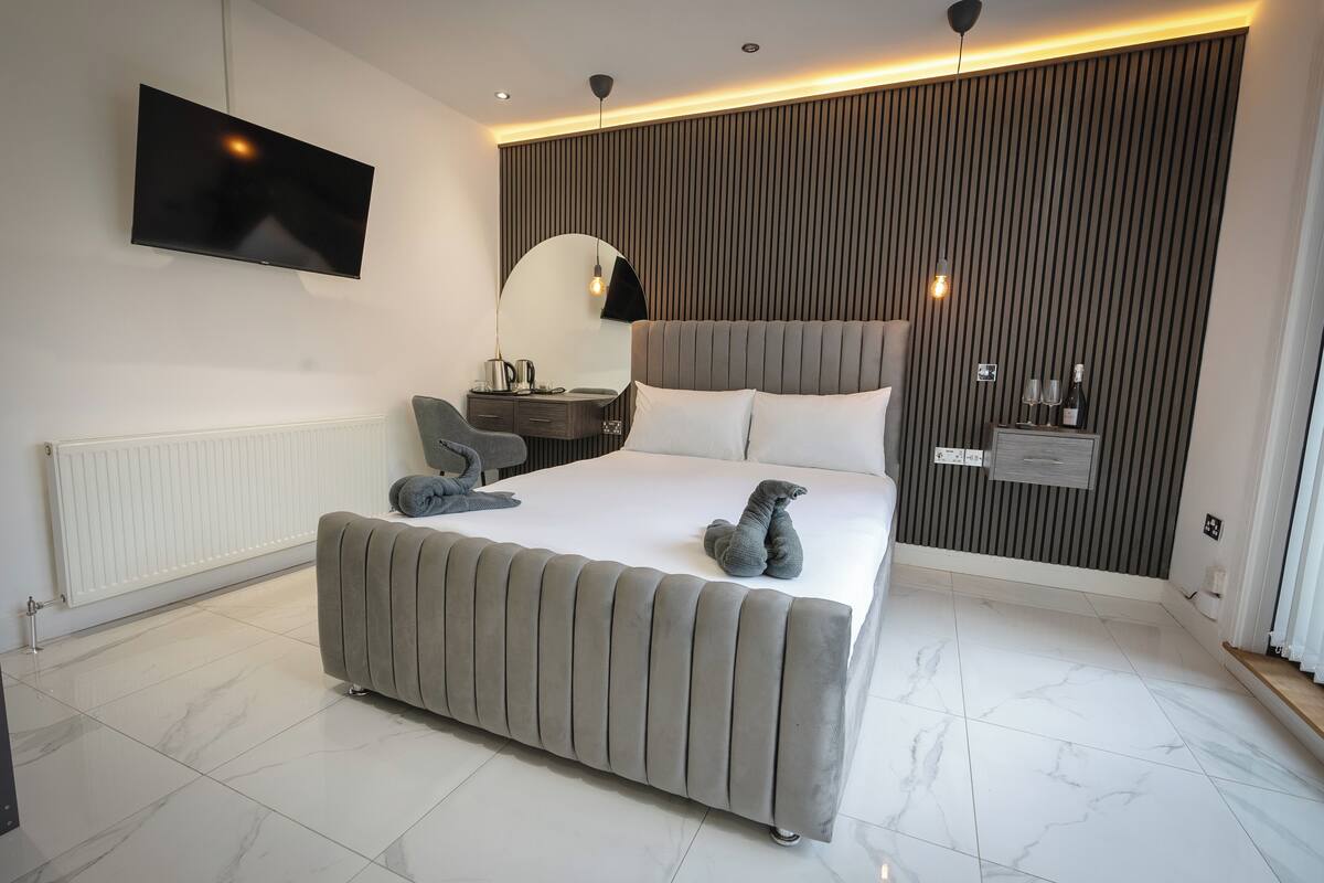Une chambre moderne avec un grand lit, un téléviseur à écran plat, une table de chevet avec une lampe et un miroir fixé au mur.