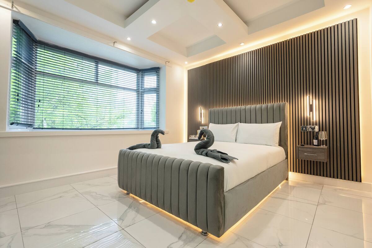 Une chambre moderne avec un grand lit, une tête de lit intégrée, une table de chevet et une lampe fixée au mur.