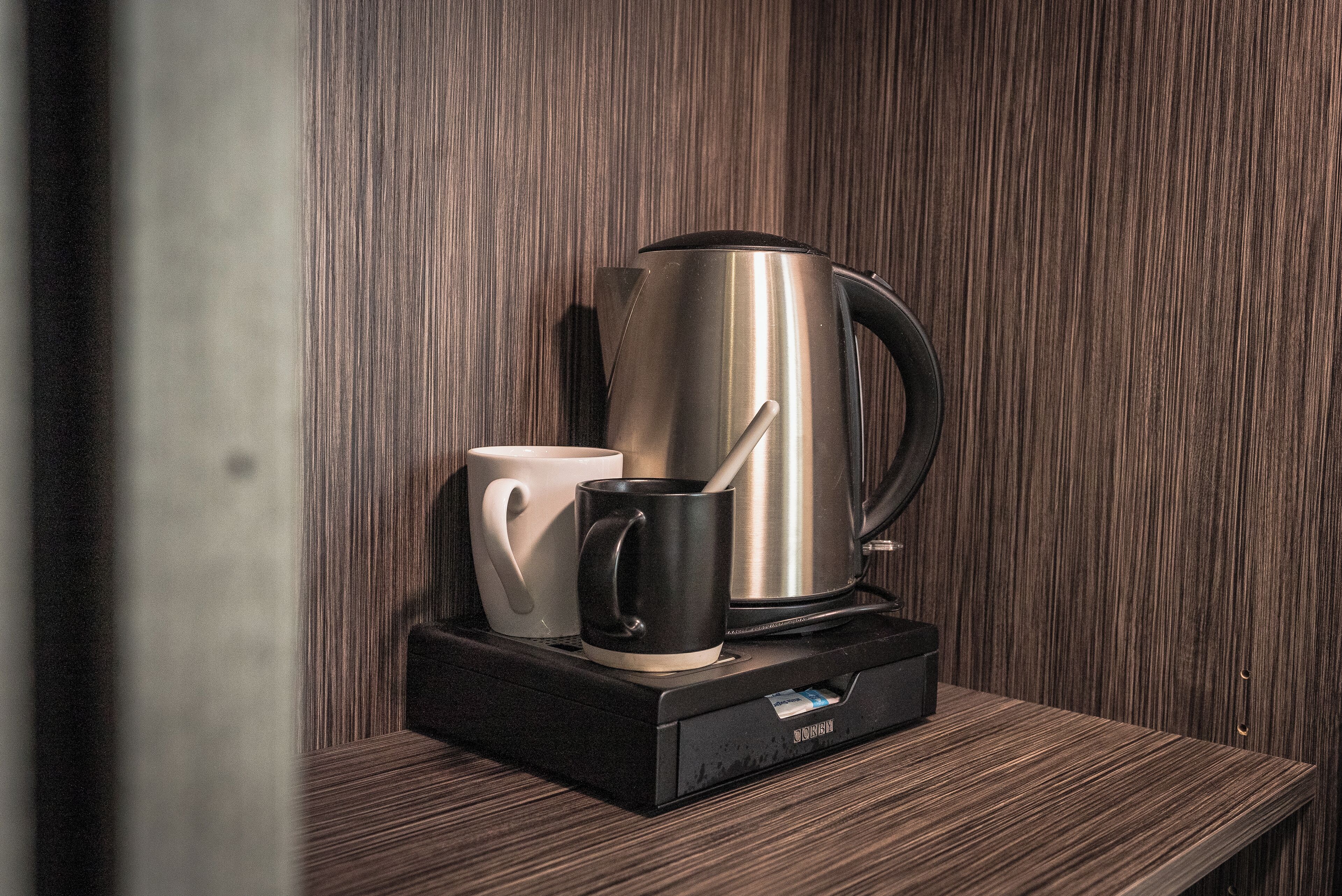 A coffee maker on a wooden table with a white mug and a black mug.