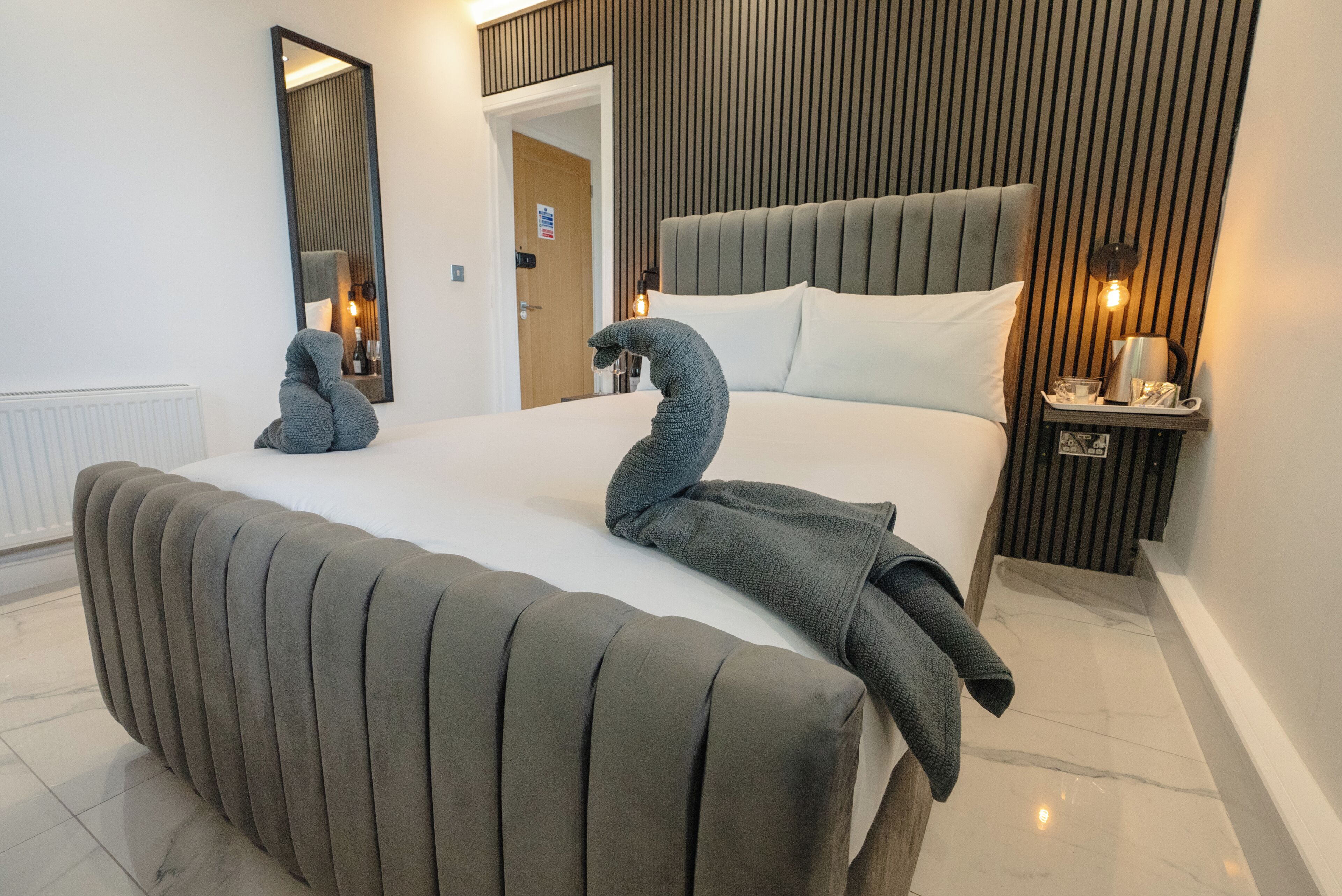 Un dormitorio moderno con una cama grande, un cabecero, una mesita de noche con una lámpara y un espejo en la pared.