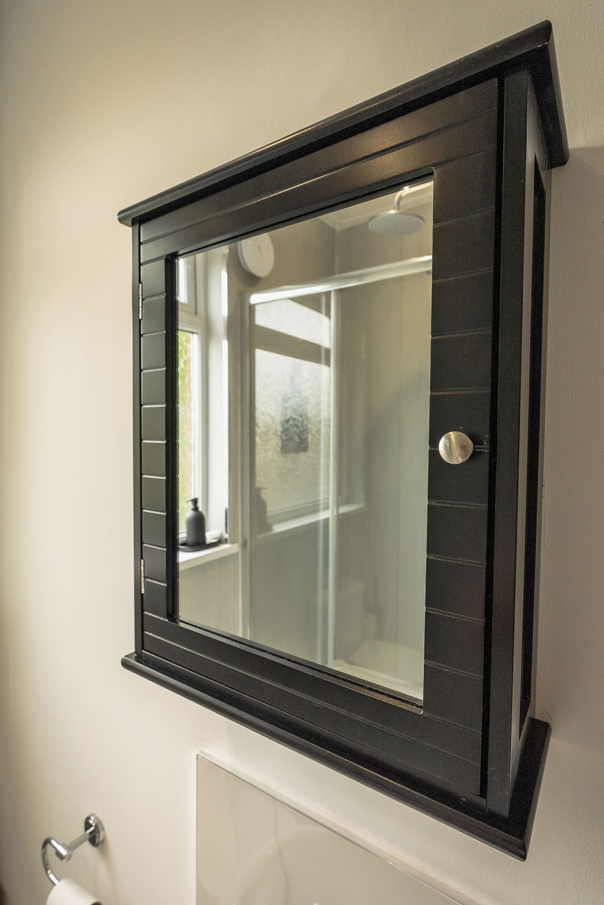 Un baño con espejo, un dispensador de papel higiénico y una ventana.