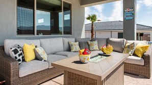 Un área de estar exterior moderna con un sofá seccional gris, sillas de mimbre y una mesa de madera.
