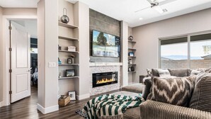 Una sala de estar moderna con chimenea, un televisor montado encima y un amplio ventanal con vistas al exterior.