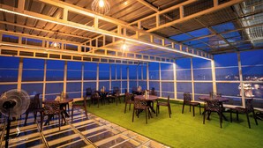 A rooftop restaurant with tables and chairs, a green carpet, and a view of the city at night. - Hotel Jsr Ganga (Varanasi)