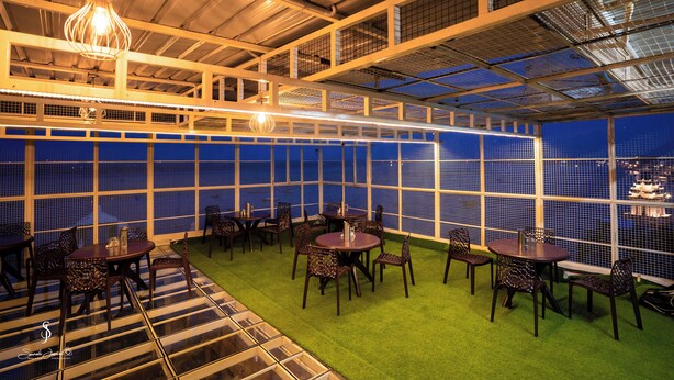 A rooftop restaurant with tables and chairs, a view of the city, and a unique ceiling design. - Hotel Jsr Ganga (Varanasi)