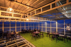 A rooftop restaurant with tables and chairs, a view of the city, and a unique ceiling design. - Hotel Jsr Ganga (Varanasi)