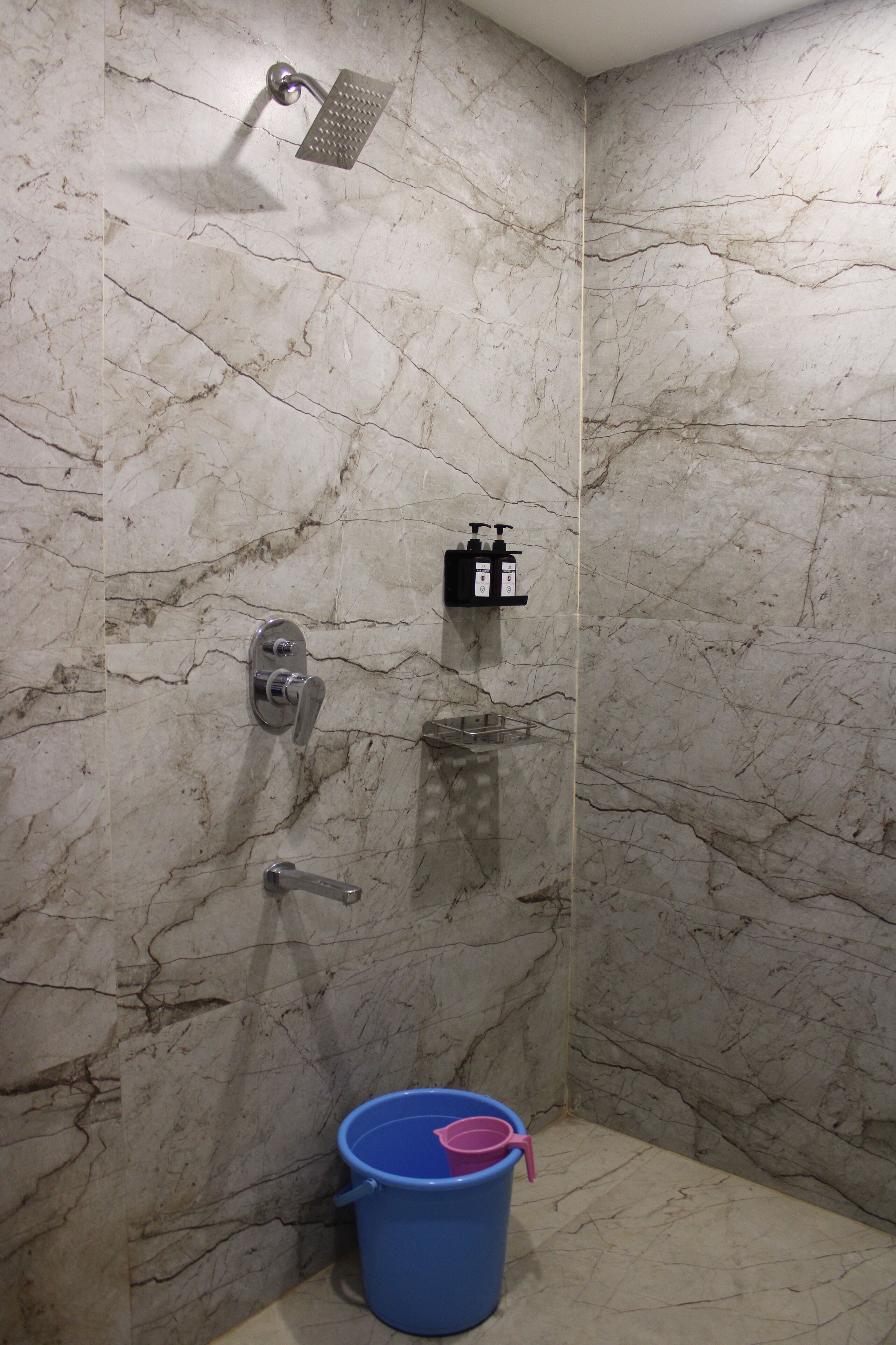 A bathroom with a shower, a sink, and a blue bucket.