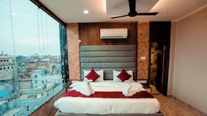 A modern hotel room with a large bed, a view of the city, and a ceiling fan. - Hotel Jsr Ganga (Varanasi)