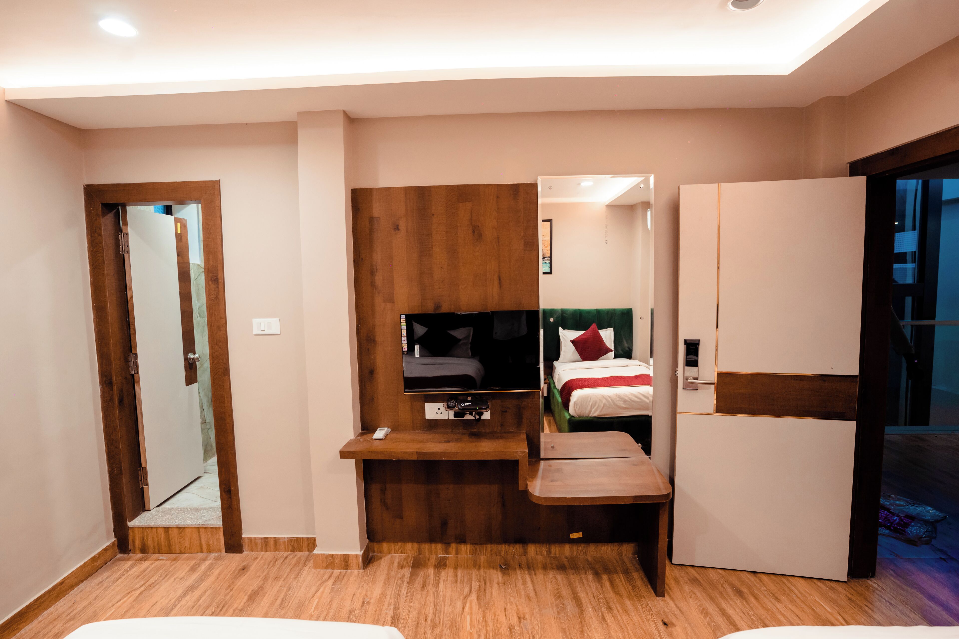 Ett modernt hotellrum med ett skrivbord i trä, en platt-TV, en säng med röda kuddar och en garderob.