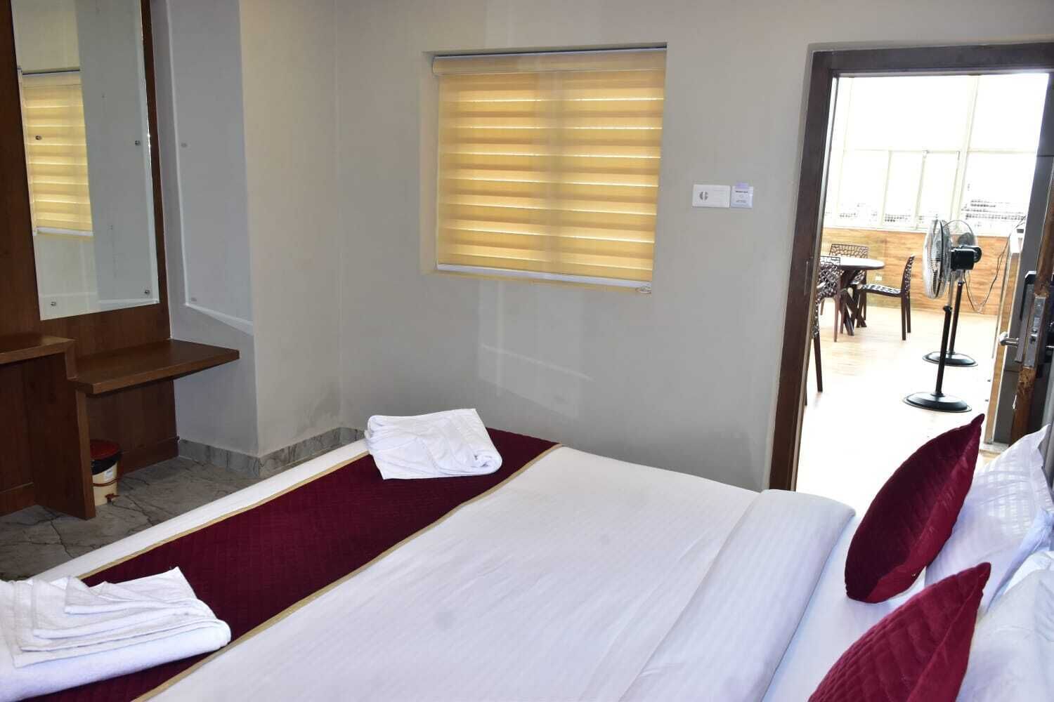 A hotel room with a bed, a wooden bench, a window with blinds, and a view of the outside.