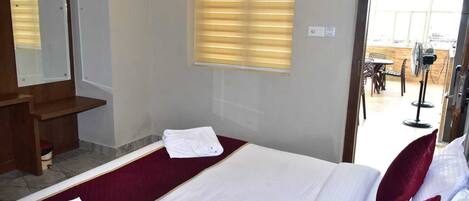 A hotel room with a bed, a wooden bench, a window with blinds, and a view of the outside.