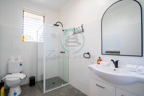 Een badkamer met een douchecabine van glas, een toilet, een wastafel met spiegel en een handdoekrek.