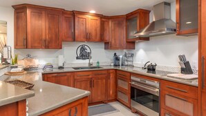 Una cocina con armarios de madera, extractor de acero inoxidable, horno empotrado y encimera de granito.