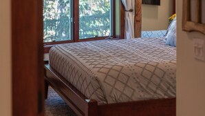 Un dormitorio con cama, ventana con cortinas, puerta y vista a árboles.