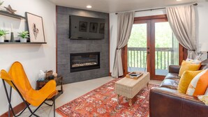 Una sala de estar con chimenea, un sofá, un sillón y un amplio ventanal con cortinas.