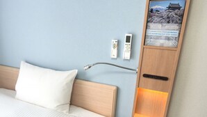 Una habitación de hotel con una cama, una mesita de noche con lámpara y un enchufe de pared.