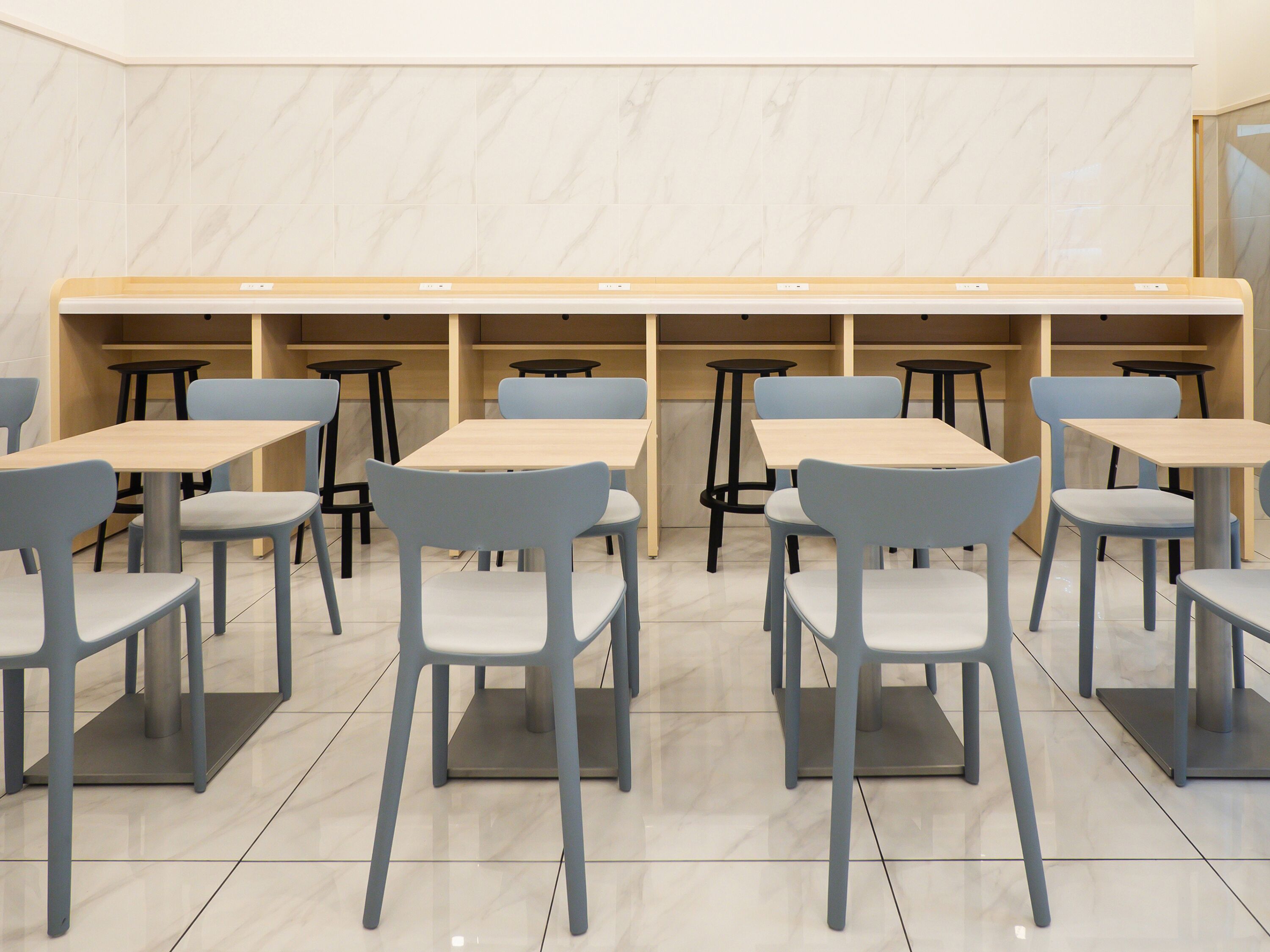Un interior de restaurante moderno con varias mesas y sillas, paredes de mármol y un diseño limpio y minimalista.