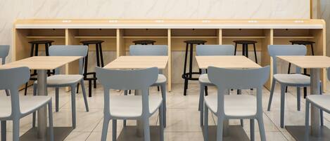 Un interior de restaurante moderno con varias mesas y sillas, paredes de mármol y un diseño limpio y minimalista.
