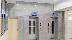 Un área de ascensores moderna, con paredes de mármol y dos ascensores, cada uno con pantalla digital.