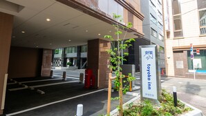 Entrada de un hotel con un cartel de 'Toyoko Inn', un camino de entrada con puerta y un pequeño jardín con plantas.