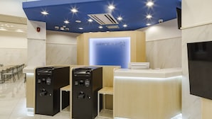 Un área de recepción de hotel moderna con una pared azul de acento, una pantalla digital y un espacio de estar con mostrador.