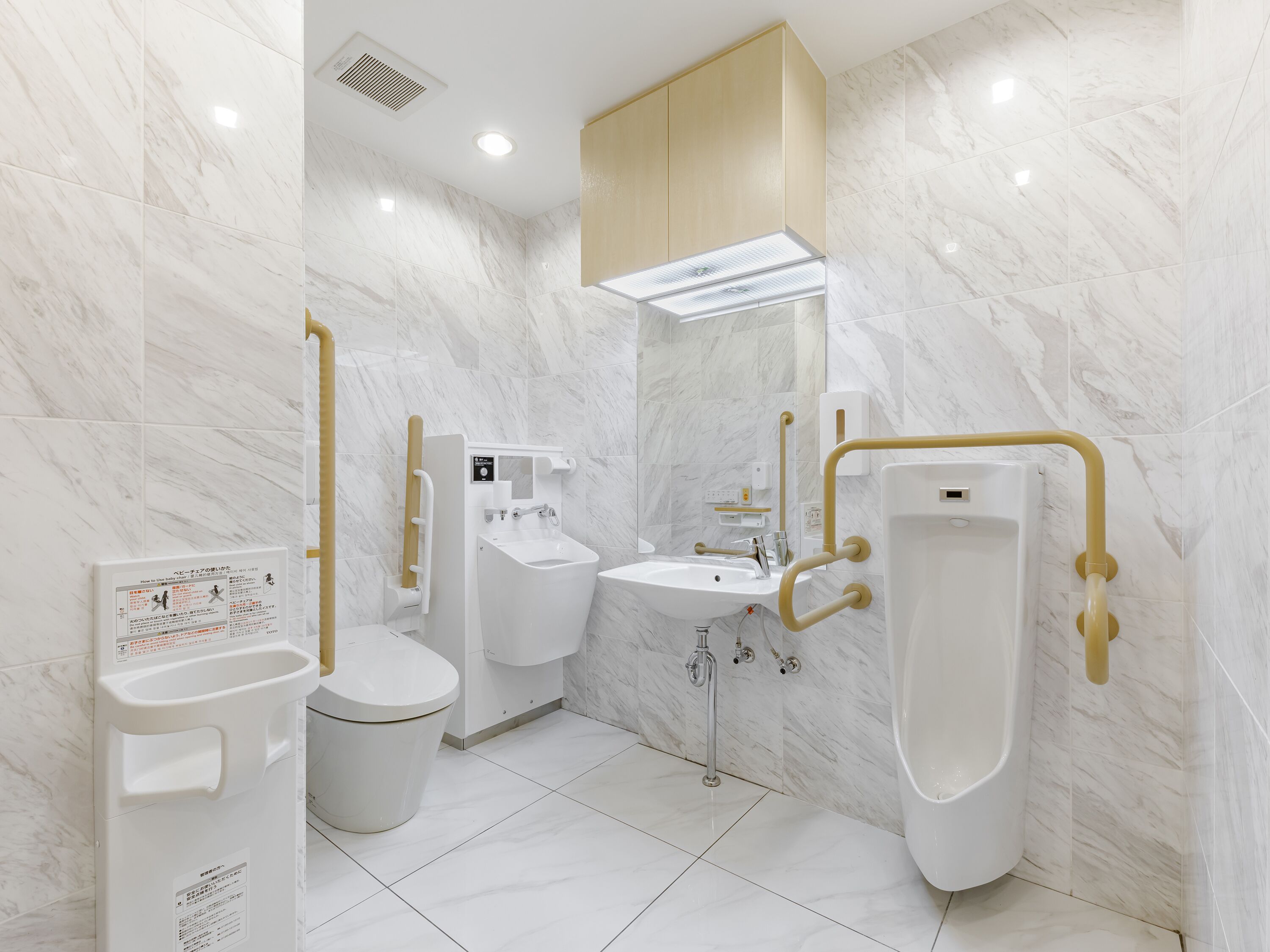A modern bathroom with a toilet, bidet, and urinal, equipped with accessibility features like grab bars and a control panel.