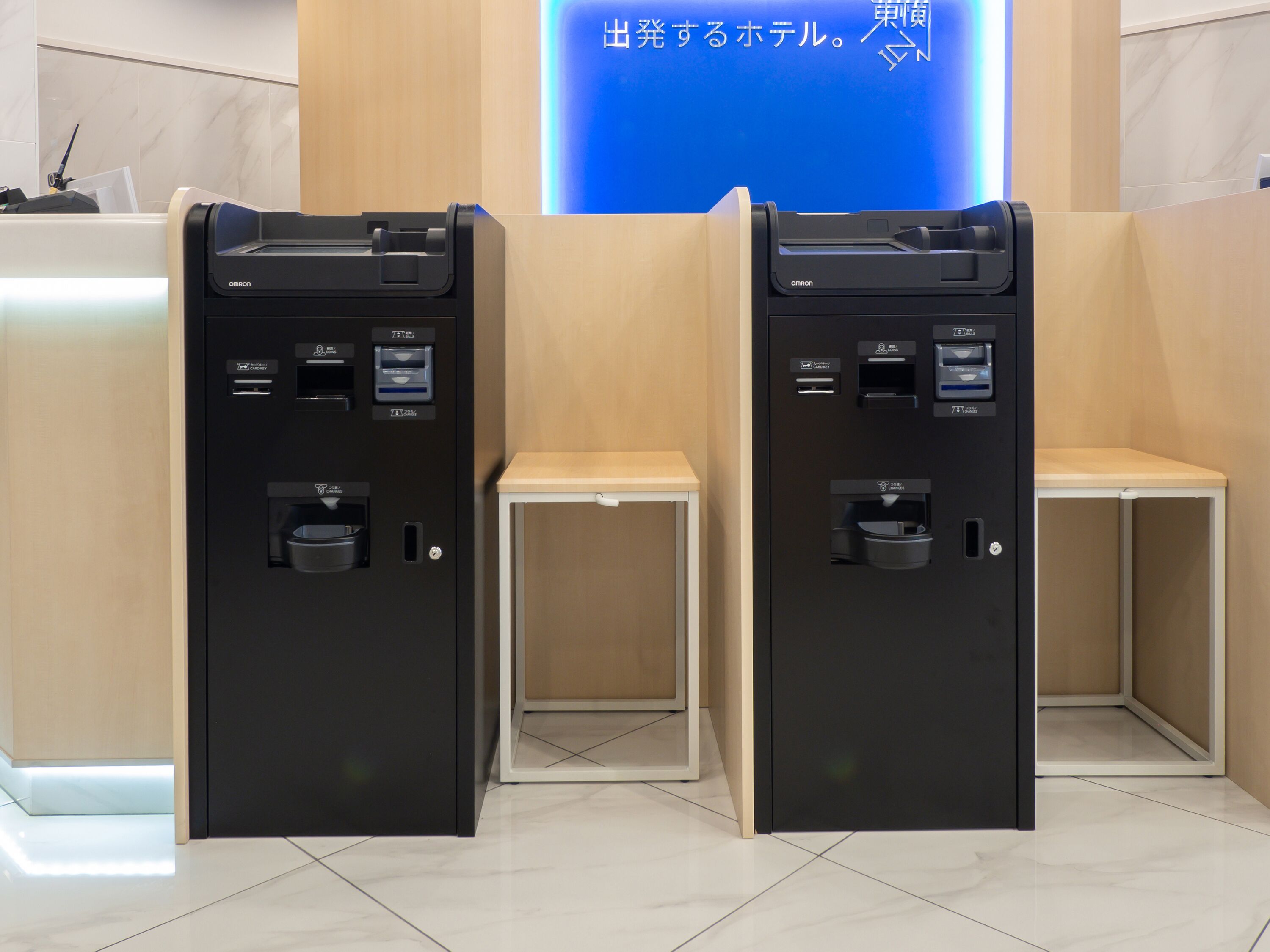 Two self-service kiosks with card payment options, a small table, and a blue illuminated sign in the background.