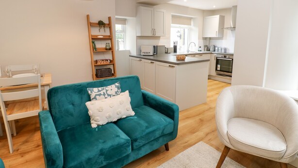 A modern living room with a teal sofa, a white armchair, and a wooden ladder shelf. - Hall Garth Cottage (Leyburn)