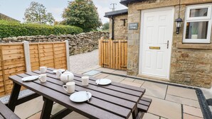 A wooden picnic table with plates and cups, a stone wall, and a cottage entrance with a door and window. - Hall Garth Cottage (Leyburn)