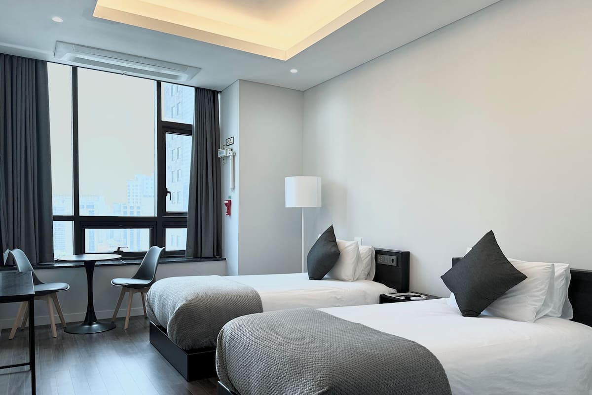 A modern hotel room with two beds, a desk, and a chair.