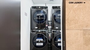 A coin laundry facility with black dryers and washers, labeled in Korean. - JD Tower Hotel (Seoul)