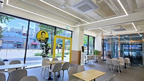 A modern cafe interior with tables and chairs, large windows, and a view of the street outside. - JD Tower Hotel (Seoul)