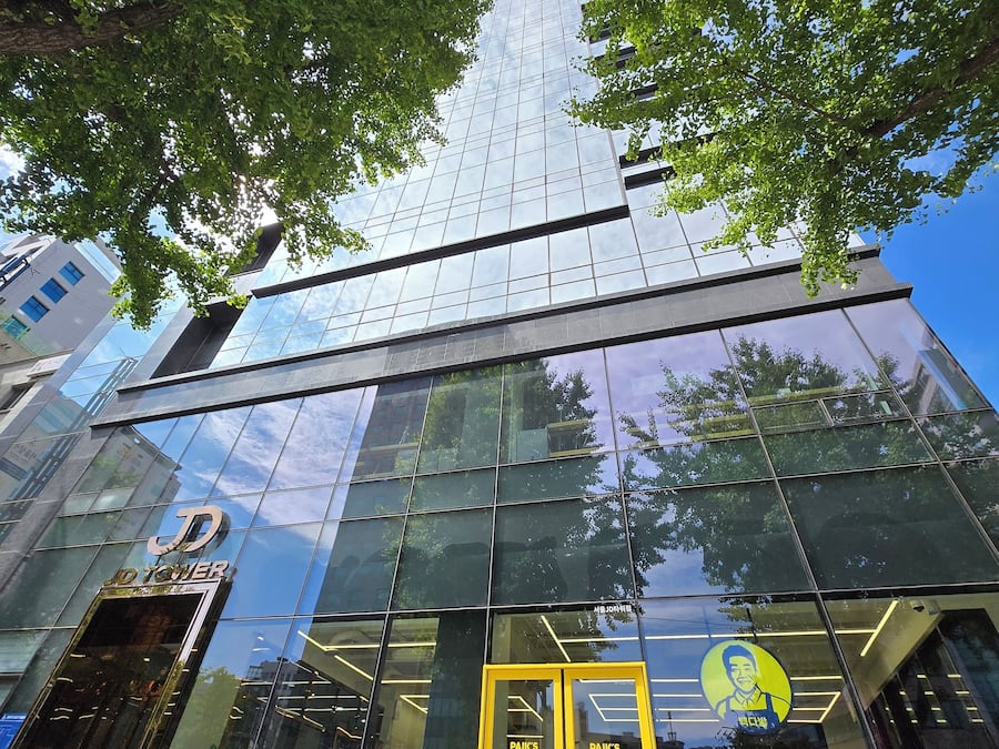 Un edificio moderno con fachada de vidrio y el logotipo visible en la entrada.