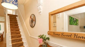 A staircase with carpeted steps, a wall clock, a mirror with a 'Home Sweet Home' sign, a wooden bench, and a vase with flowers. - Station Avenue (Sandown)