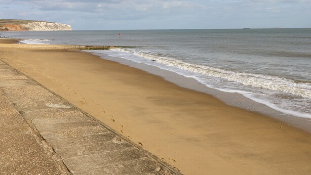 A beach with a concrete walkway and cliffs in the background. - Station Avenue (Sandown)