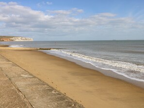 A beach with a concrete walkway and cliffs in the background. - Station Avenue (Sandown)