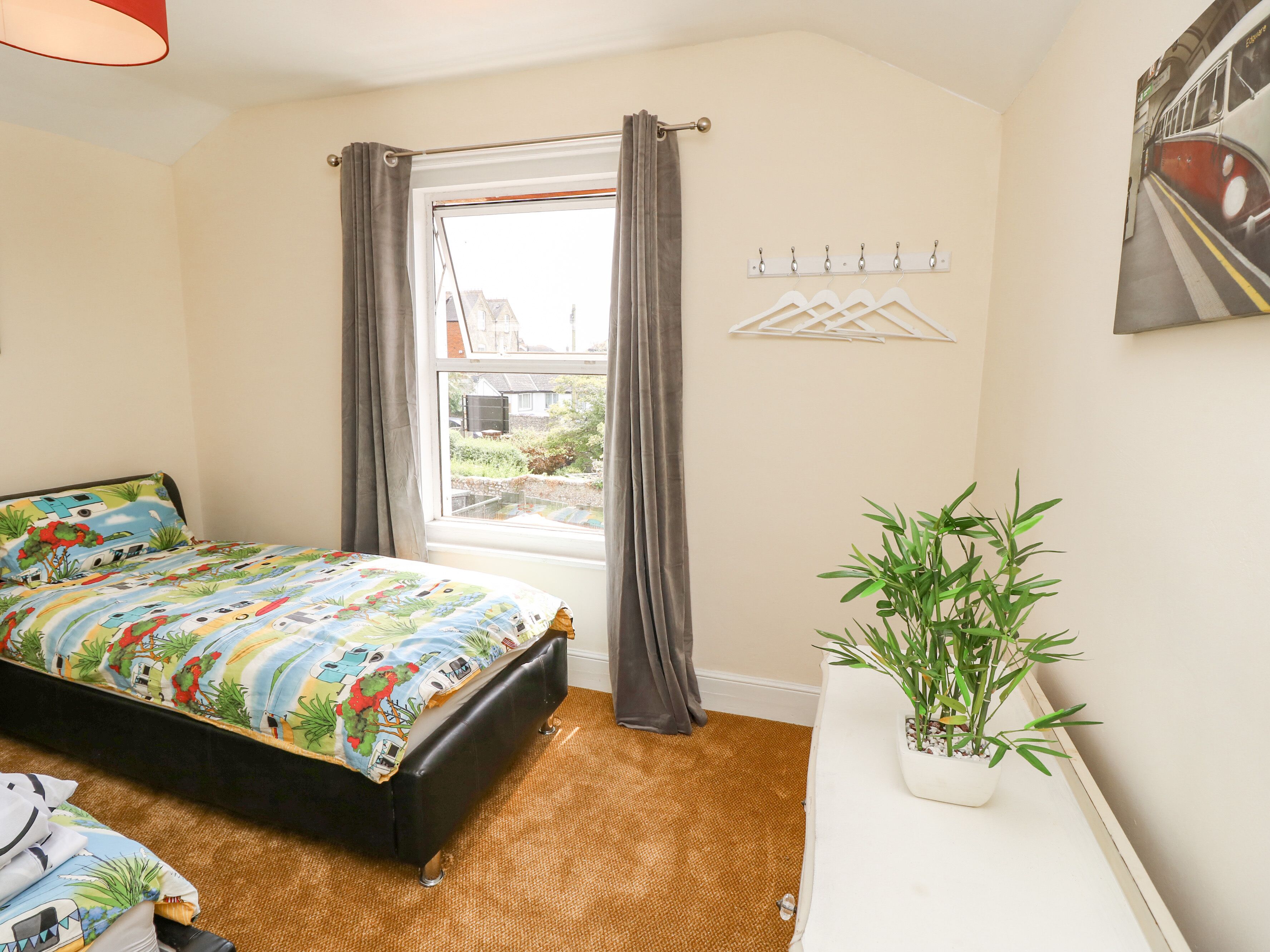 A bedroom with a bed, a window with curtains, a wall-mounted coat rack, and a potted plant.