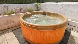 A wooden hot tub in an outdoor setting with a concrete floor and a white wall in the background. - Station Avenue (Sandown)