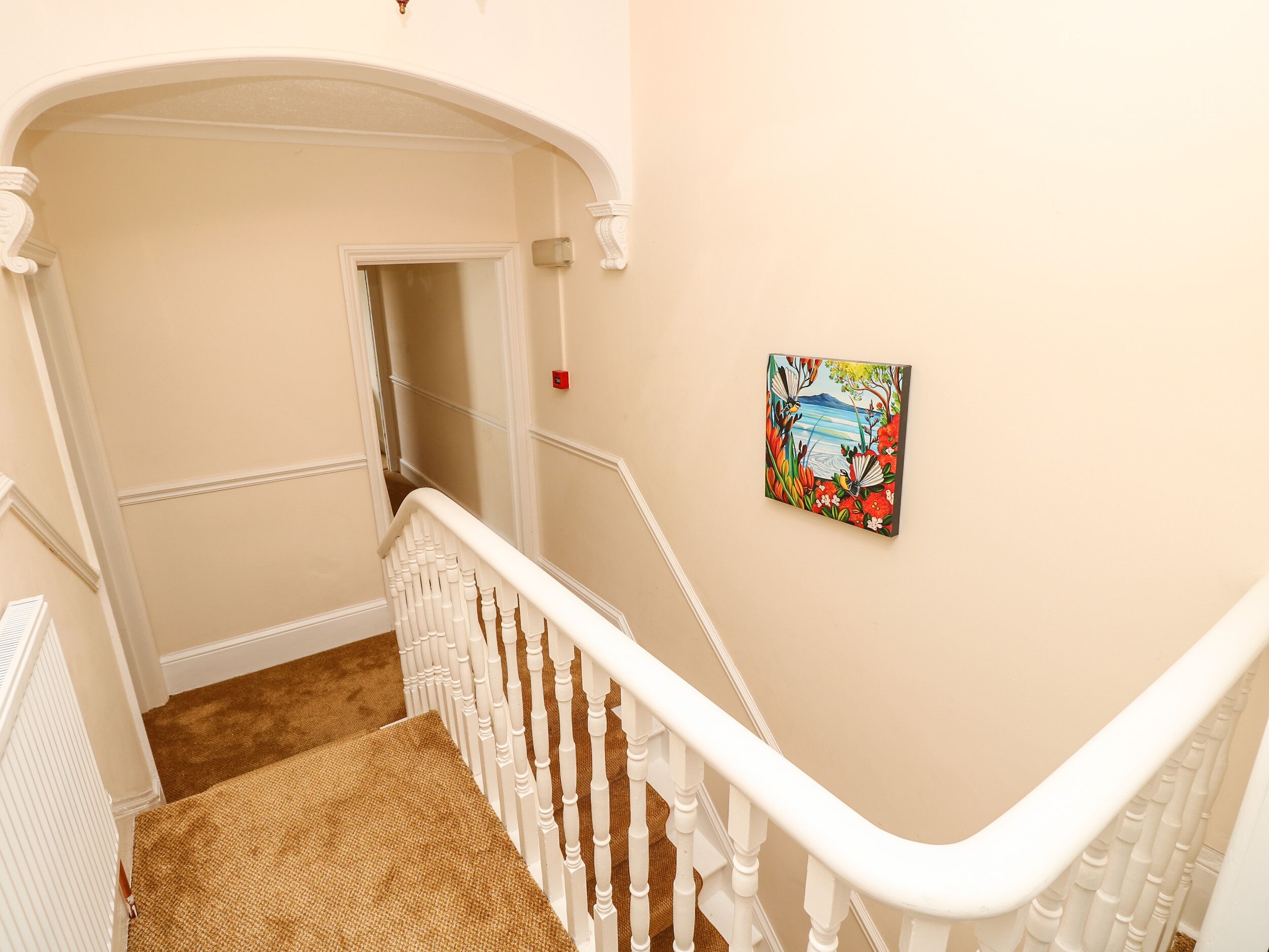 A staircase with white balusters, a woven carpet, and a painting on the wall.