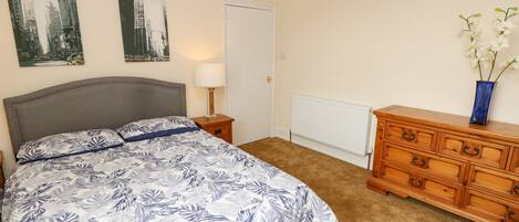 A bedroom with a bed, a nightstand, a dresser, a radiator, and two wall art pieces.