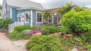 A quaint house with a porch, surrounded by lush greenery and a garden. - 16 Village Run... 2 Bedroom Condo by RedAwning (Warren)