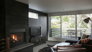 A modern living room with a fireplace, a television, and a large window overlooking a deck. - 16 Village Run... 2 Bedroom Condo by RedAwning (Warren)