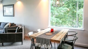 A modern dining area with a wooden table, black chairs, a red candle, and a view of trees through a large window. - 16 Village Run... 2 Bedroom Condo by RedAwning (Warren)