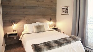 A bedroom with a wooden headboard, two bedside tables with lamps, a bed with white bedding, a gray fur throw, and a framed picture on the wall. - 16 Village Run... 2 Bedroom Condo by RedAwning (Warren)